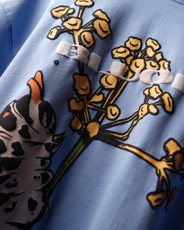Close-up of a light blue garment featuring a large graphic print of a black-and-white spotted caterpillar and yellow flowers with green stems.