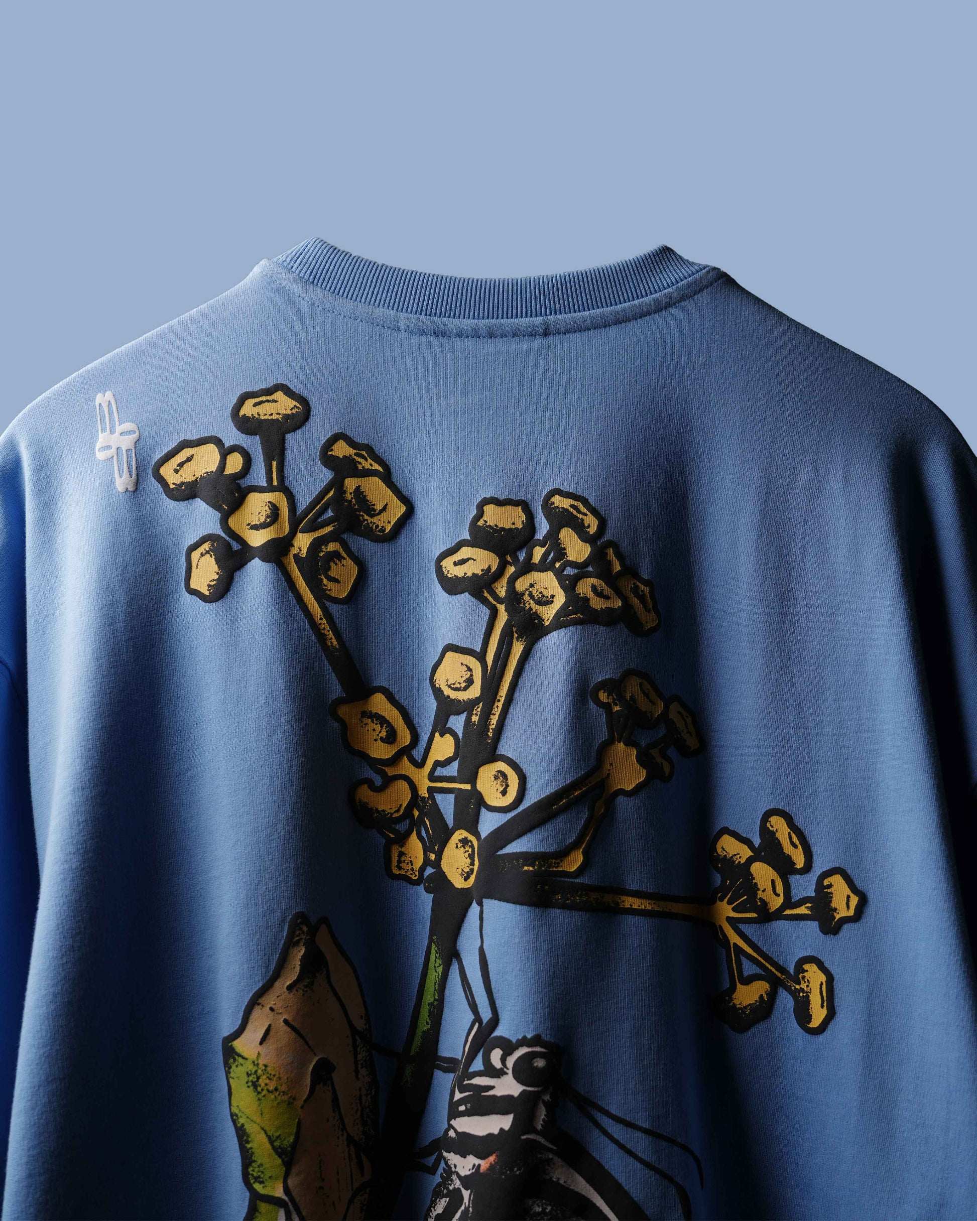 Close-up of the back of a blue crewneck T-shirt featuring a large graphic print of yellow flowers and a butterfly.