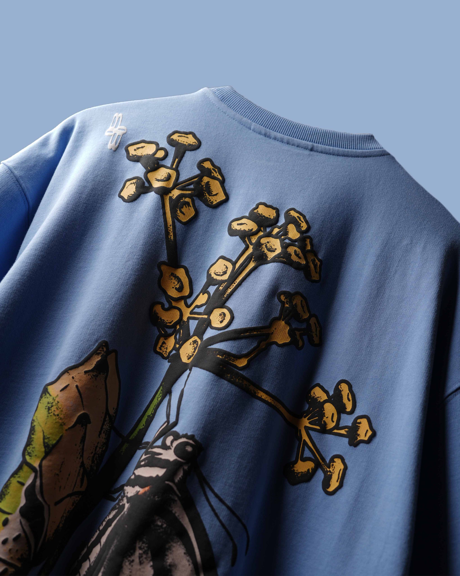 Close-up of the back of a light blue crewneck sweatshirt featuring a large graphic print of yellow flowers and a butterfly in brown, green, and black.