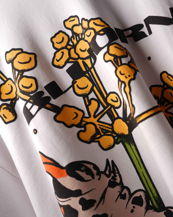 Close-up of a white graphic t-shirt featuring a stylized illustration of yellow flowers with black outlines, green stems, and a cow print with orange and black accents.