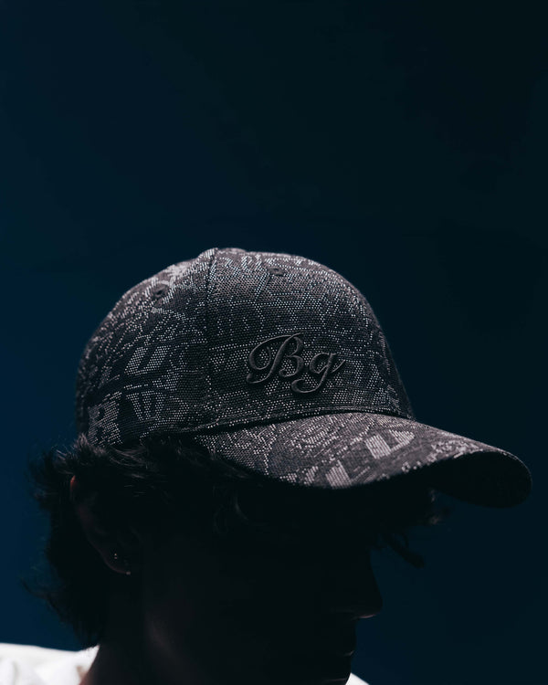A close-up side profile of a person wearing a dark patterned baseball cap with an embroidered 'B&G' logo on the front, set against a very dark navy background.